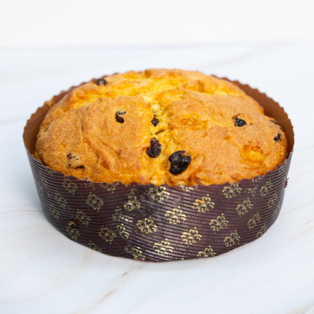 Panettone con uvetta e canditi nel pirottino marrone decorato, vista frontale su piano in marmo