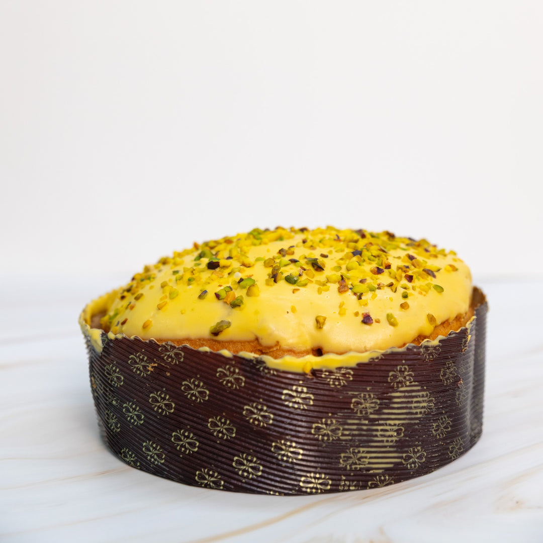 Panettone con copertura gialla e granella di pistacchio, vista frontale ampia su sfondo chiaro