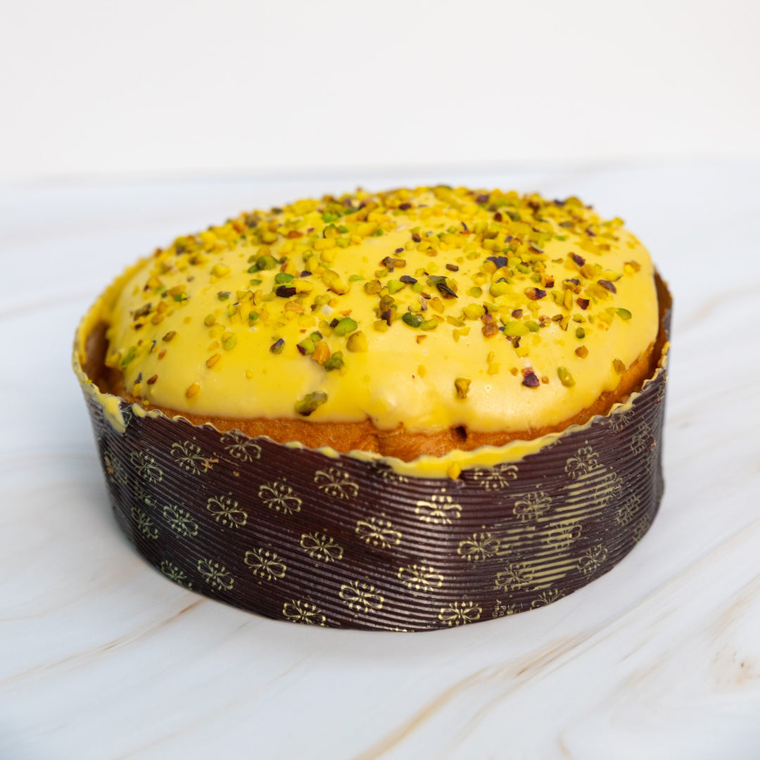 Panettone con copertura gialla e granella di pistacchio, vista frontale a distanza