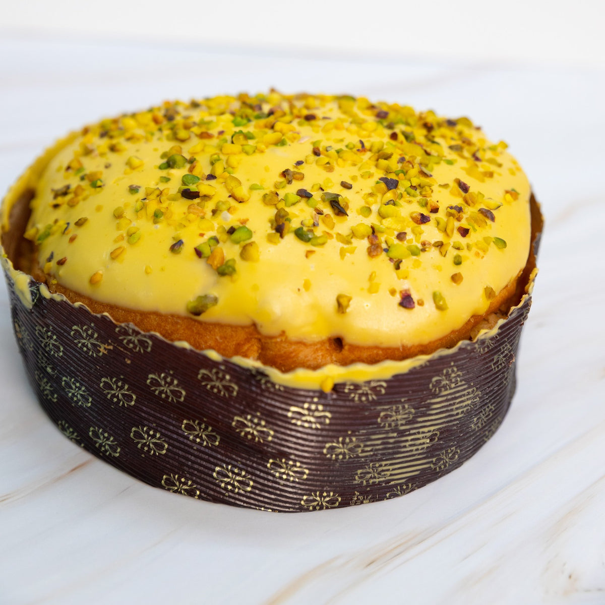Panettone con copertura gialla e granella di pistacchio nel pirottino decorato, vista frontale