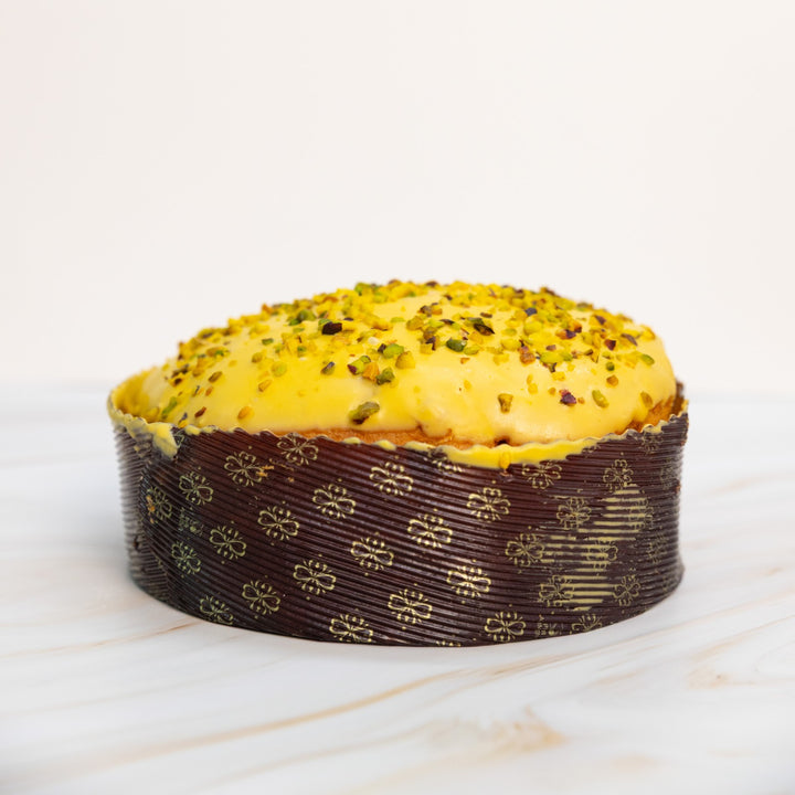 Panettone con copertura gialla e granella di pistacchio, vista frontale ampia su sfondo chiaro